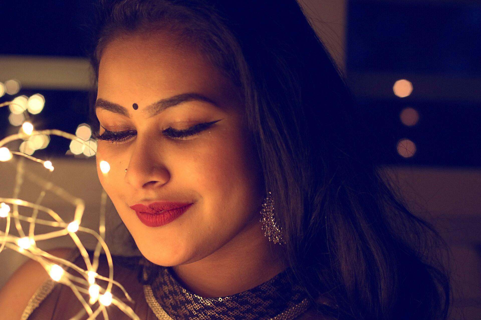 Portrait of a smiling woman adorned with lights and elegant jewelry, creating a warm, glamorous atmosphere.